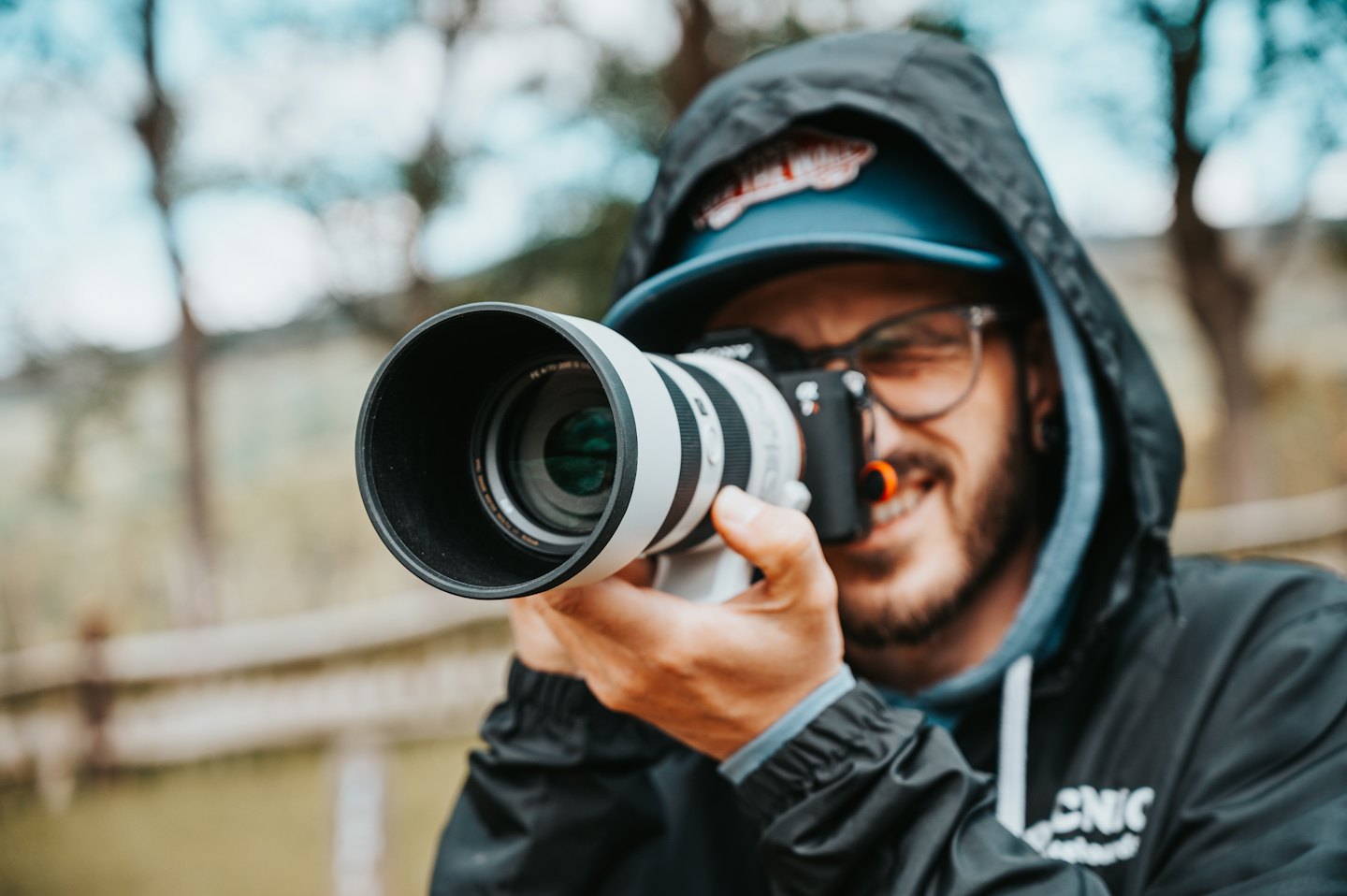 A photographer wearing a blue cap holds a white camera.