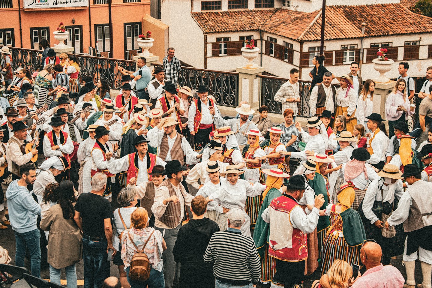 A street festival crowd in folk costumes with string instruments and dancing.