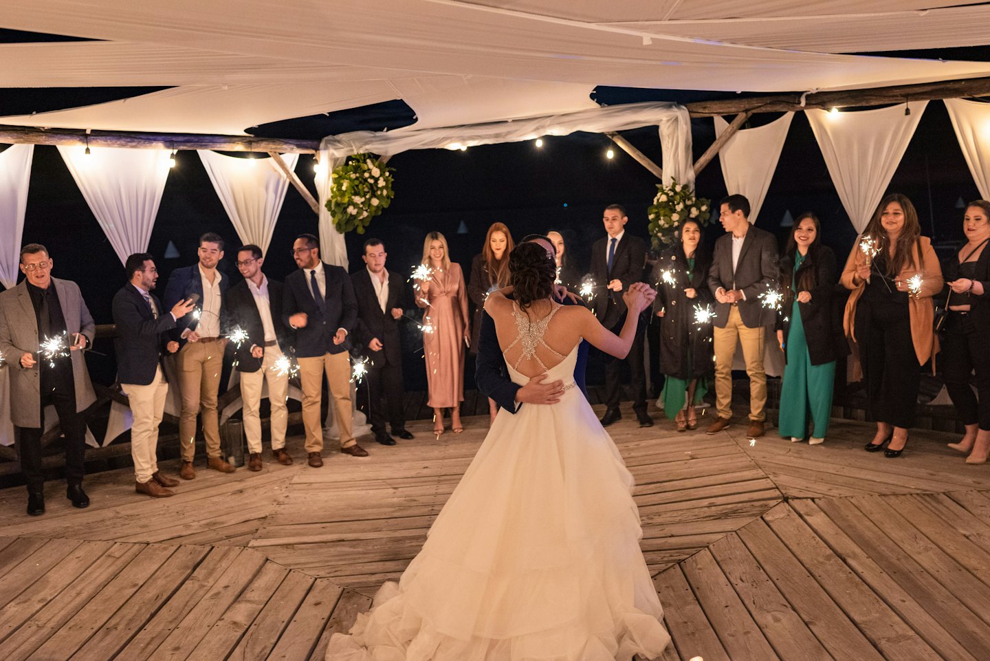 Wedding guests hold lit sparklers while the couple dances outdoors.