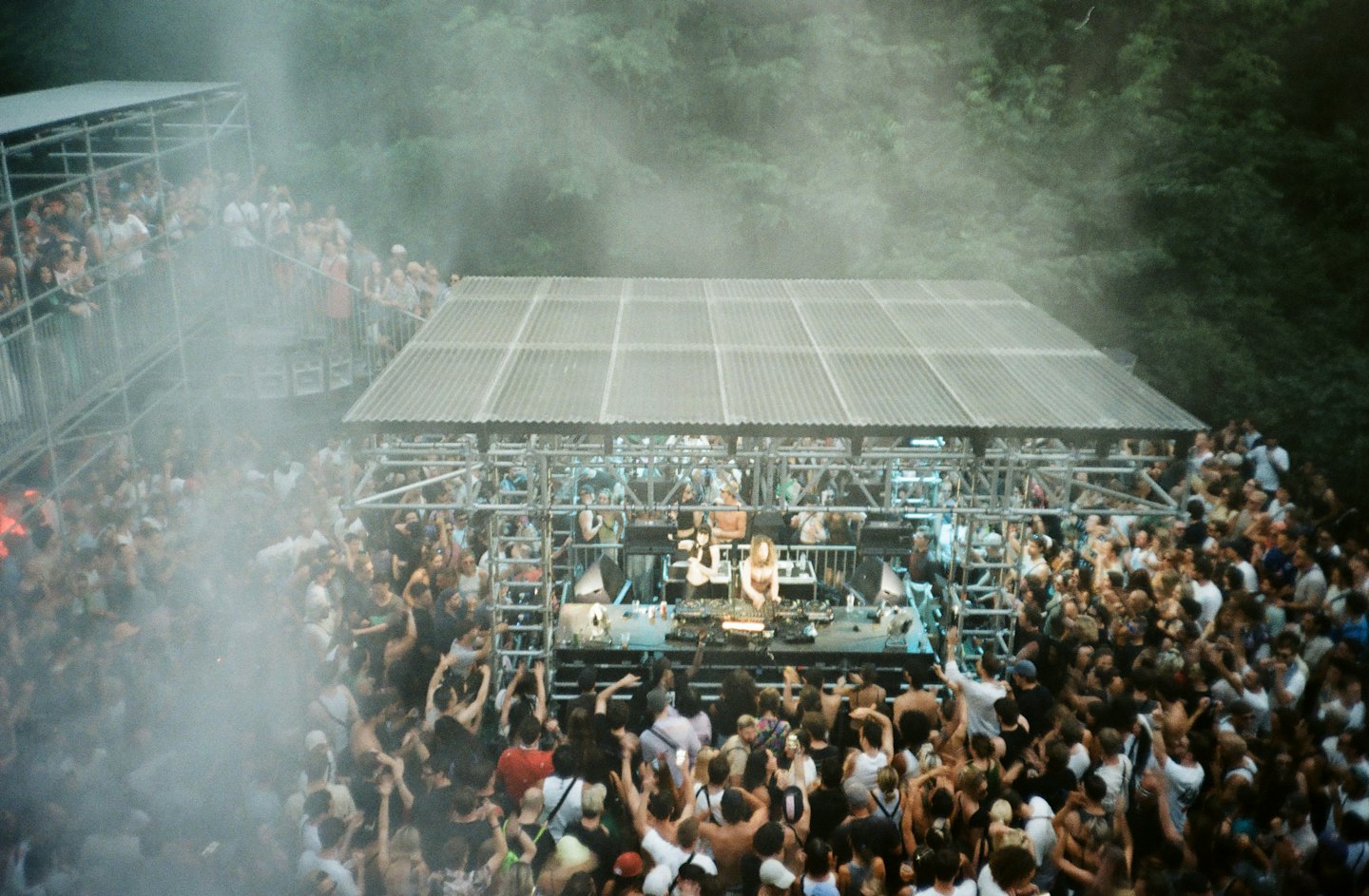 Crowd dancing at an outdoor music festival with DJs on stage.